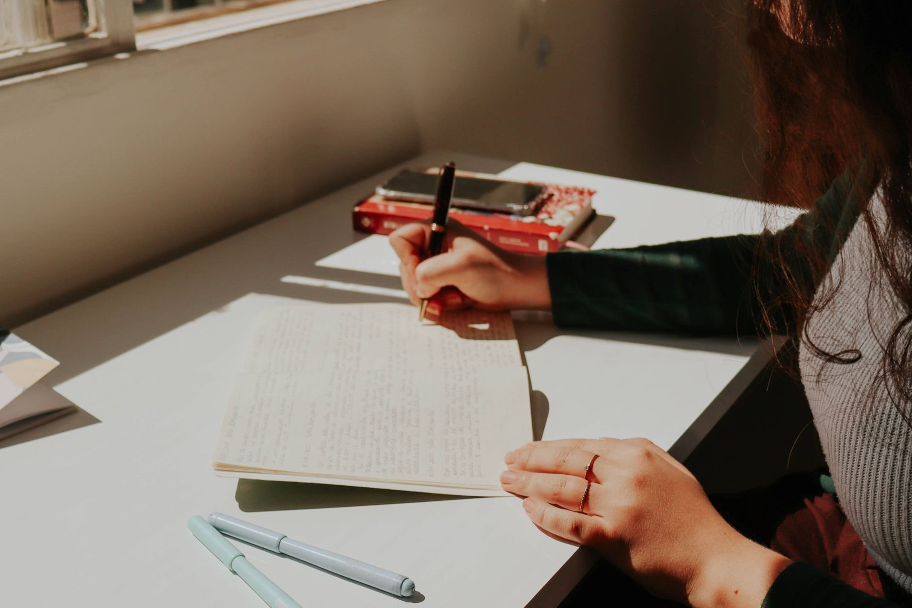 Young woman writing in a notebook by a sunlit window, creating a warm and focused atmosphere.